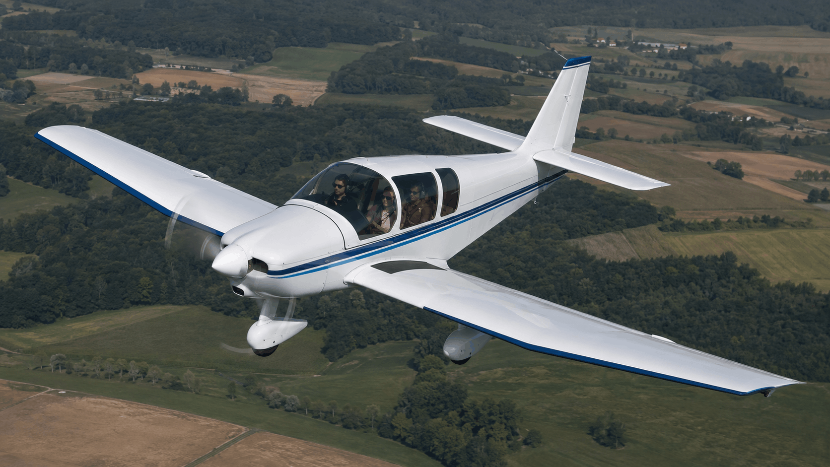 Classic Robin-style four-seat aircraft parked beside a grass runway