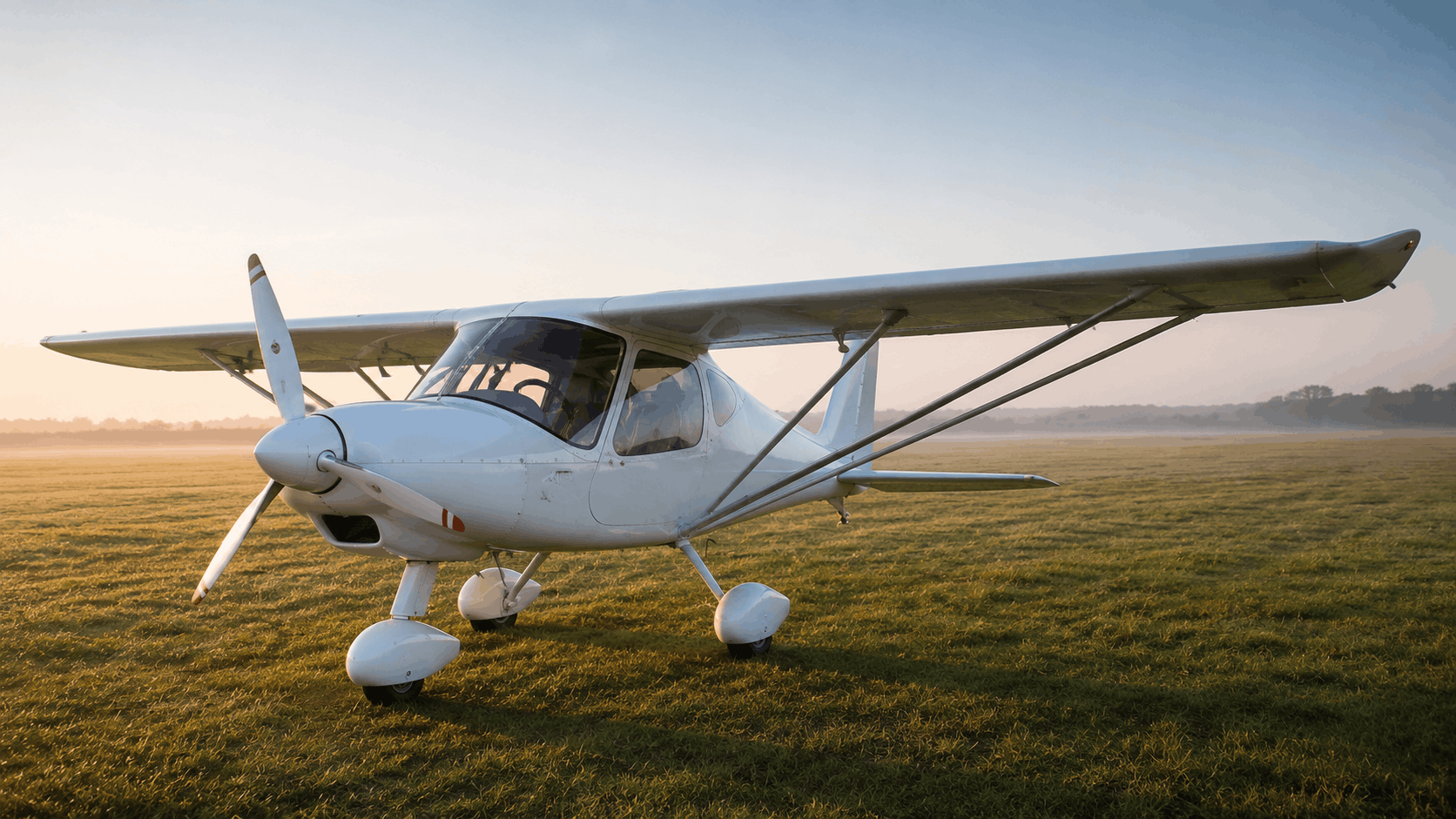 Unmarked Ikarus C42-style light aircraft on a grass airfield at sunrise