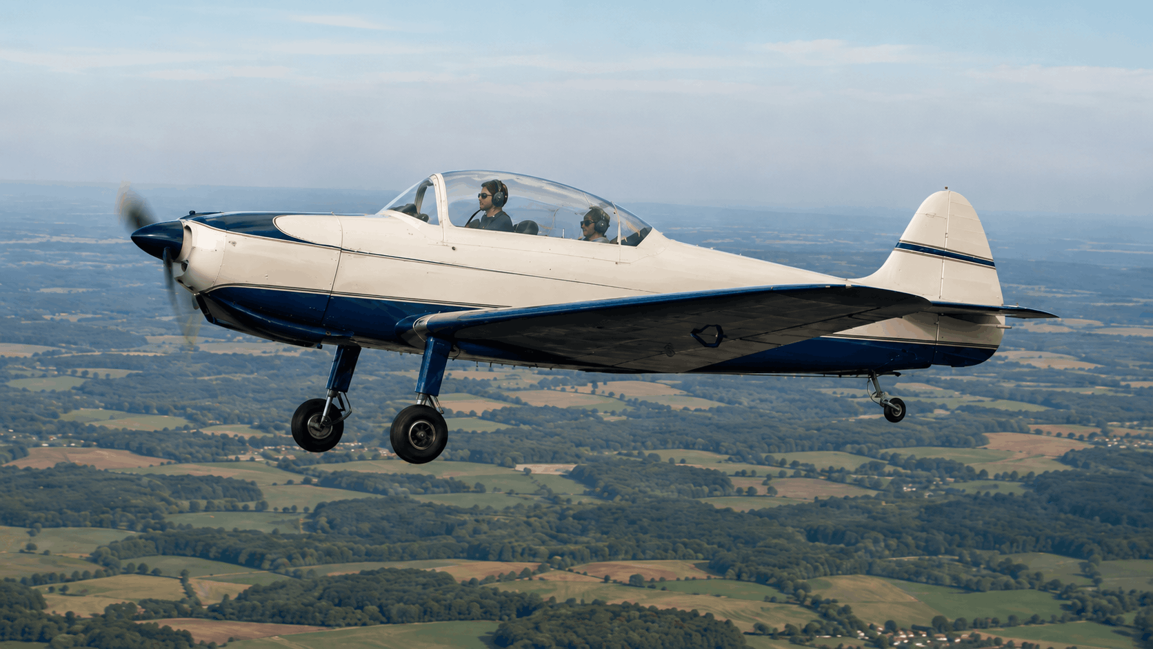 AI-generated UTVA Aero 3-style vintage trainer aircraft in flight over countryside
